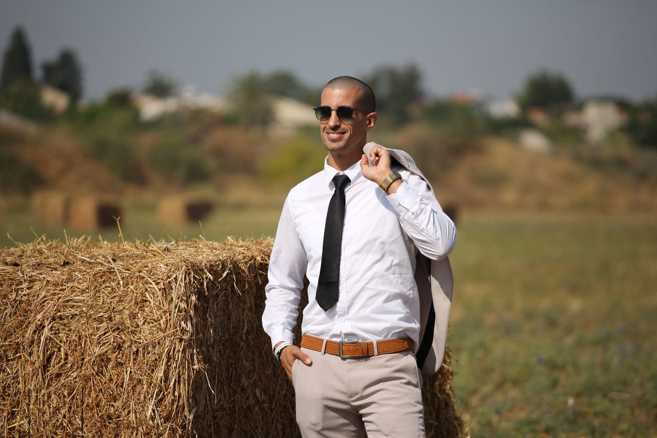 gallery-03 Confident man in sunglasses with suit jacket, smiling in a hay field.