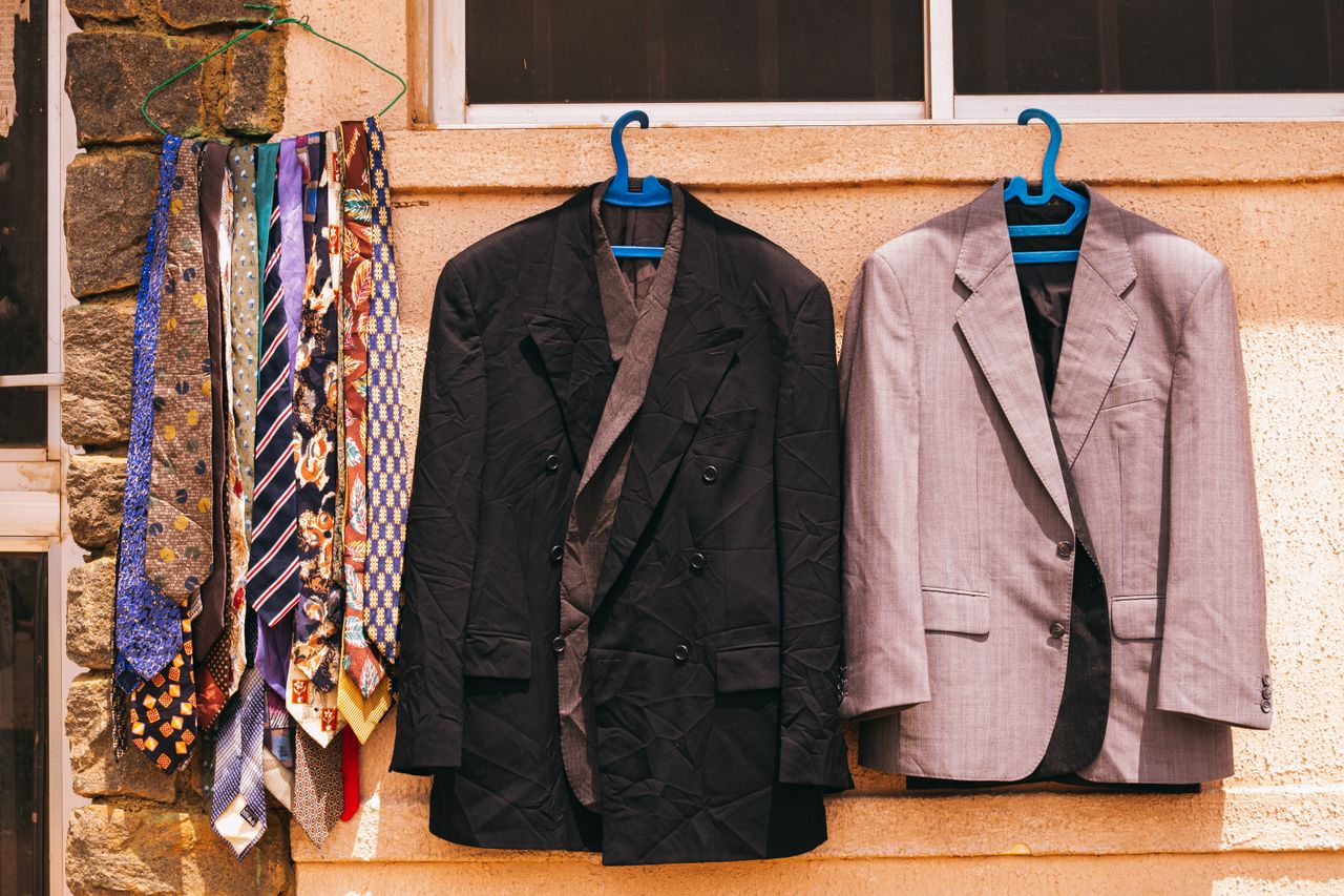 home-img A black and gray suit with colorful ties hanging outdoors on a wall in Jos, Nigeria.