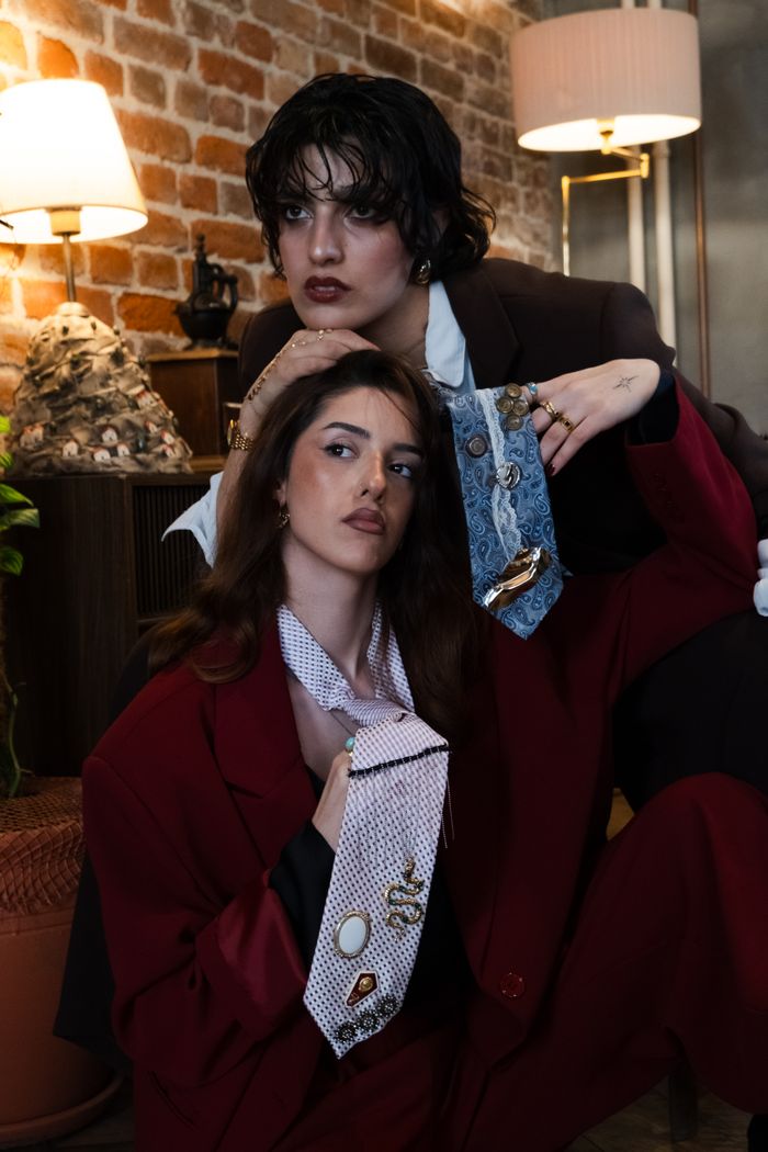 gallery-05 Two fashionable adults posing indoors with trendy suits and ties, exuding a modern artistic vibe.